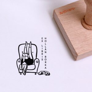 Ex libris pecsét, fotelben, lábával a háttámlán, hanyatt fekve olvasó lányt, és a fotel mellett, fekvő kutyát ábrázoló grafikával. Nyeles fa alapra készült, gumi lenyomattal, egyedileg megadott névvel készült.