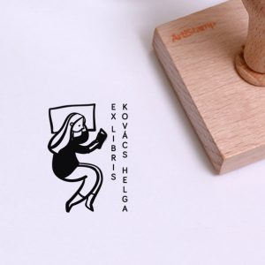 Ex libris pecsét, párnán, oldalt fekvő és olvasó lányt ábrázoló grafikával. Nyeles fa alapra készült, gumi lenyomattal, egyedileg megadott névvel készült.