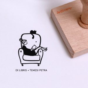 Ex libris pecsét, fotelben ülő, lábbal a karfán olvasó lányt, és a háttámlán fekete macskát ábrázoló grafikával. Nyeles fa alapra készült, gumi lenyomattal, egyedileg megadott névvel készült.
