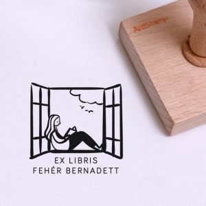 Ex libris pecsét, nyitott ablakban ülő és olvasó lányt, a háttérben felhőt és két repülő madarat ábrázoló grafikával. Nyeles fa alapra készült, gumi lenyomattal, egyedileg megadott névvel készült.