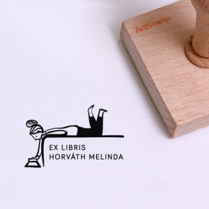Ex libris pecsét, hason fekvő, olvasó lányt ábrázoló grafikával. Nyeles fa alapra készült, gumi lenyomattal, egyedileg megadott névvel készült.