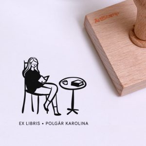Ex libris pecsét, asztal mellett, széken ülő, kávézó, olvasó lányt ábrázoló grafikával. Nyeles fa alapra készült, gumi lenyomattal, egyedileg megadott névvel készült.