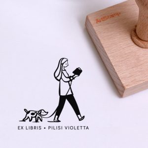 Ex libris pecsét, kutyát sétáltató, olvasó lányt ábrázoló grafikával. Nyeles fa alapra, gumi lenyomattal, egyedileg megadott névvel készült.