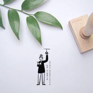 Ex libris pecsét, utazó, fogódzkodóba kapaszkodó, olvasó lányt ábrázoló grafikával. Nyeles fa alapra készült, gumi lenyomattal, egyedileg megadott névvel készült.